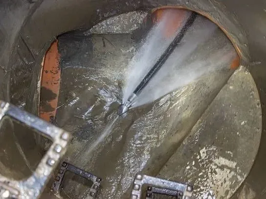 A hydro jetting nozzle spraying high-pressure water into a sewer pipe inside a pit