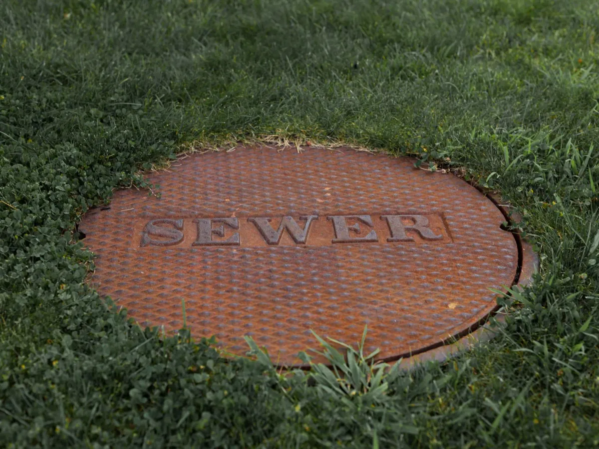 A round cast-iron cover marked SEWER set into a lawn