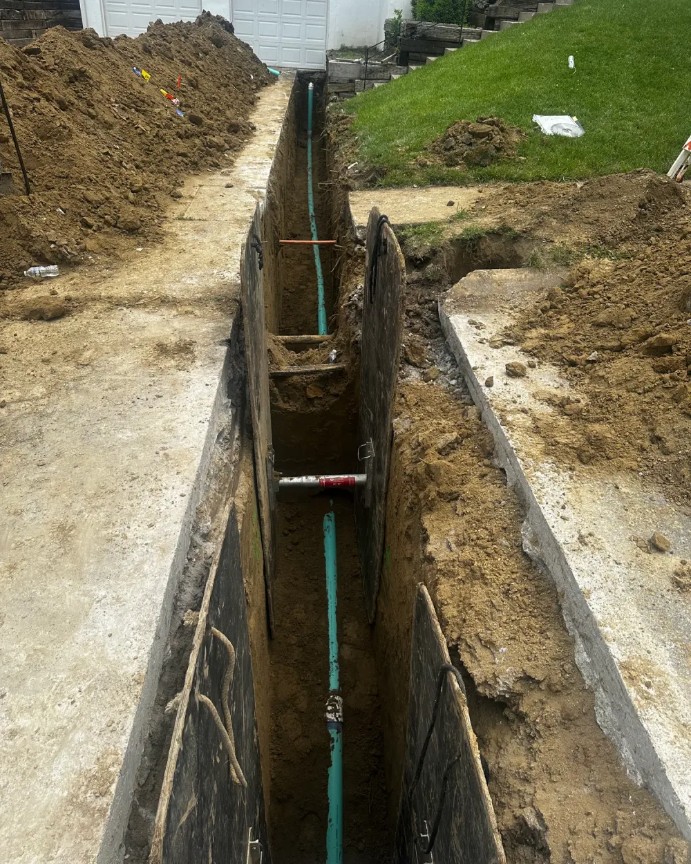 A shored trench along a house with a new sewer pipe laid in the bottom