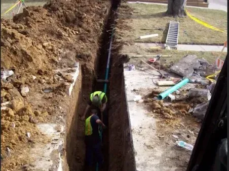 A worker standing in a deep sewer trench dug beside a house