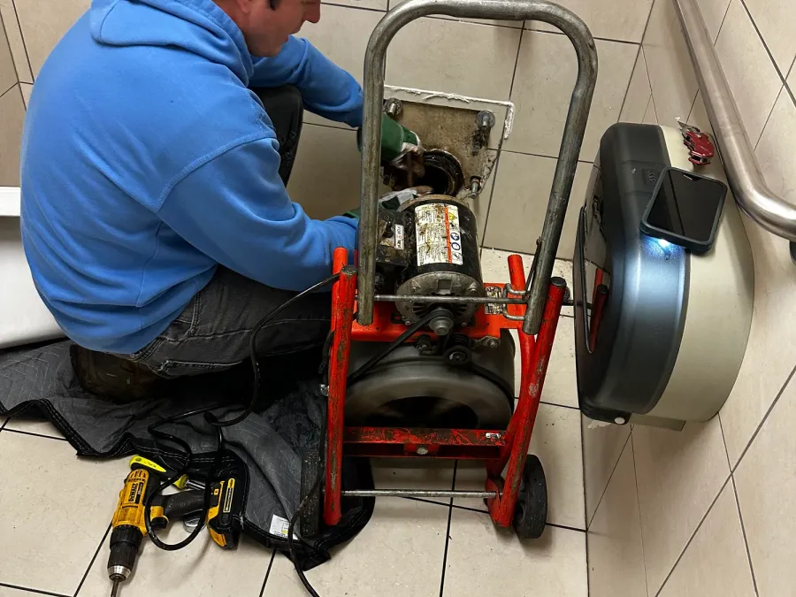 A technician in a blue hoodie running a drum drain machine into a wall clean-out
