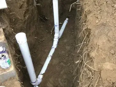 New white PVC sewer pipe and a clean-out riser laid in an open trench