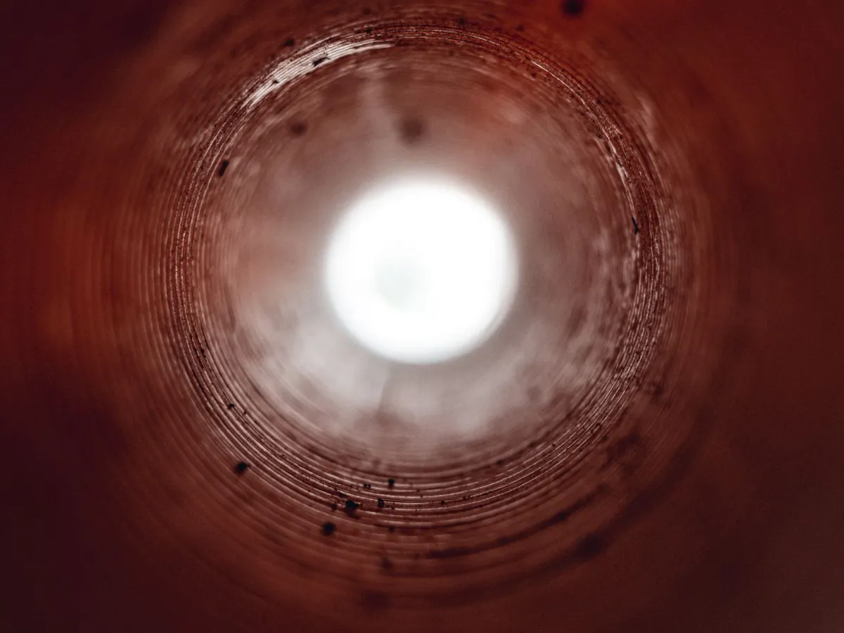 The view down the inside of a round pipe toward a bright opening at the far end