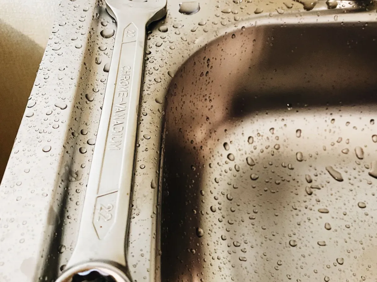 A wrench resting on the edge of a wet stainless steel kitchen sink